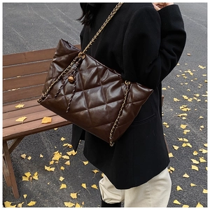 Detail of dark brown quilted PU leather bag with gold chain strap in autumn outdoor setting