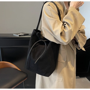 Detail of a minimalist black suede bucket bag with leather drawstring on a trench coat model