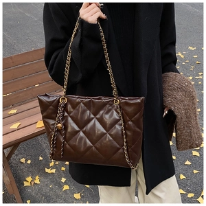 Close-up of a brown quilted faux leather tote bag with a golden chain strap in autumn