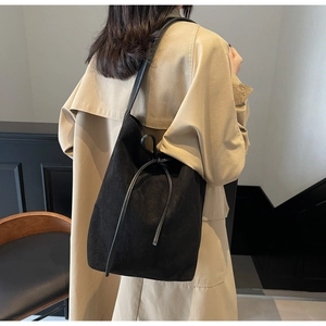 Detail of minimalist black nylon drawstring bucket bag styled with a khaki trench coat