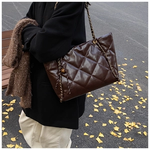 Detail of dark brown quilted PU leather tote bag with chain strap and gold ball charm