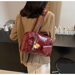 Détail d'un sac à main en cuir PU rouge foncé avec charm de baseball porté par un mannequin