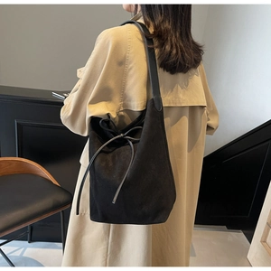 Detail of a large black suede tote bag with a leather bow on a model in a trench coat