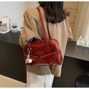 Détail du sac à main en cuir verni bordeaux avec rivets industriels et breloque baseball
