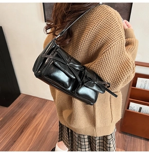 Detail of a shiny black PU underarm bag featuring front flap pockets and leather bows