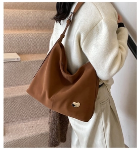 Detail of a large brown leather tote bag featuring a polished metallic bean-shaped buckle