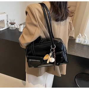 Détail d'un sac à bandoulière en similicuir noir brillant avec un pendentif baseball