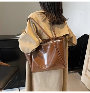 Dettaglio della borsa tote marrone lucida con lettere in rilievo indossata con trench