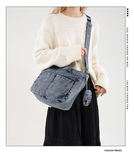 Détail d'un sac bandoulière en denim bleu avec poches externes et charm rond zippé