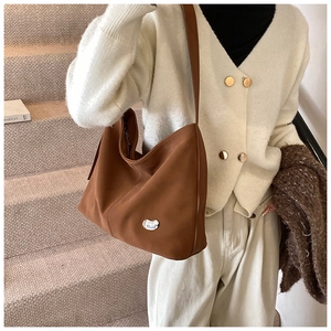 Brown faux suede crescent tote bag with silver logo detail worn over the shoulder