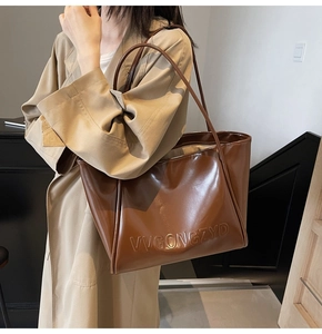 Dettaglio della borsa tote in pelle lucida marrone con ampio spazio e logo in rilievo