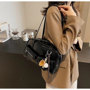 Détail d'un sac bandoulière en cuir PU noir avec breloque baseball sur veste beige