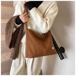 Brown leather tote bag featuring a heart charm shown on a stylish indoor staircase