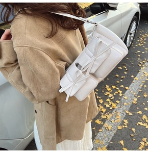 Detailed close-up of a white PU leather shoulder bag with decorative bow flap pockets