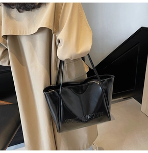 Dettaglio della borsa tote nera lucida con logo VVGONGZYD a rilievo indossata a spalla