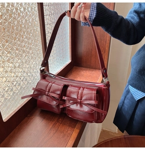 Detail view of burgundy PU leather shoulder bag with vintage bows on a wooden surface
