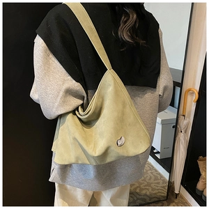 Detail of light green suede tote bag with silver heart charm shown on shoulder