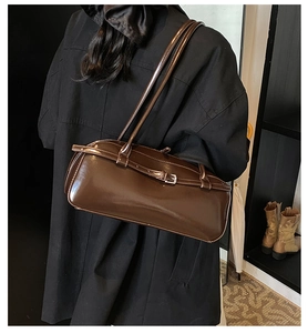 Detail of dark brown glossy baguette bag with adjustable buckle strap and shiny finish