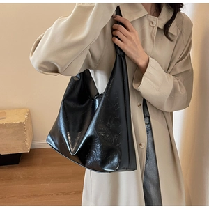 Détail du grand sac cabas noir brillant plissé porté sur un trench-coat beige