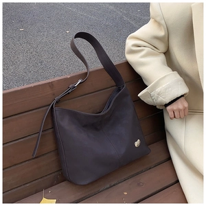 Detail of dark brown faux leather crossbody bag featuring a golden heart logo and strap