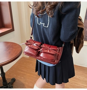 Detail view of burgundy PU leather shoulder bag with vintage bow pockets on model