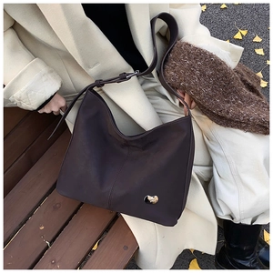 Detail of dark brown matte PU leather tote bag with heart metal buckle in autumn park