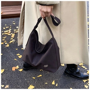 Detail of dark brown leather tote bag with metal logo on ginkgo leaves background