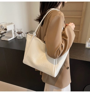Dettaglio della borsa tote in pelle color crema con lettere goffrate indossata da modella