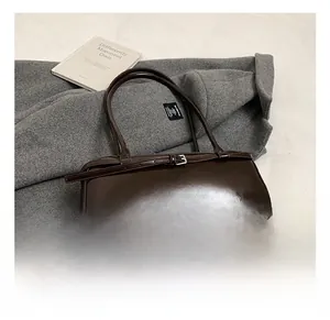 Detailed close-up of dark brown glossy patent leather shoulder bag with buckle decor