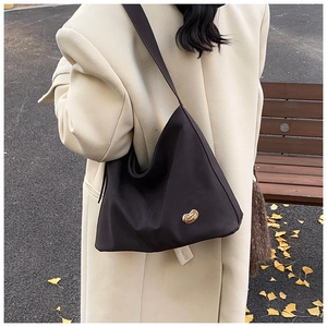 Detail of a black hobo shoulder bag with golden bean hardware on an autumn street