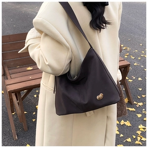 Detailed view of dark brown PU leather Hobo bag on shoulder with autumn leaf background