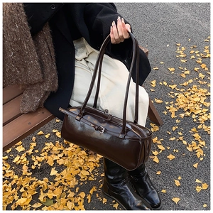 Chocolate brown faux leather shoulder bag with sleek metallic buckle on a park bench