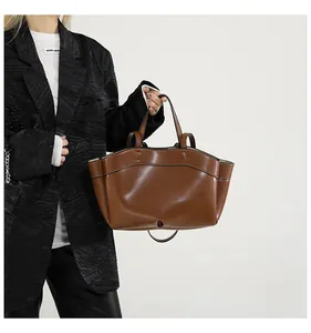 Detail of a large brown leather tote bag with black contrast stitching and shoulder straps