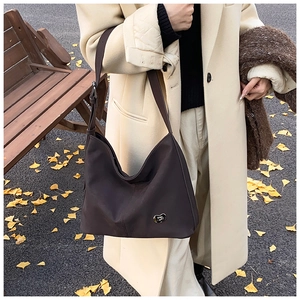Detail of dark brown leather hobo bag featuring a golden heart logo on fall background