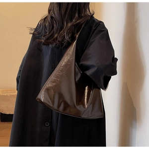 Détail de la texture cuir verni froissé du sac à bandoulière marron foncé dans un cadre moderne
