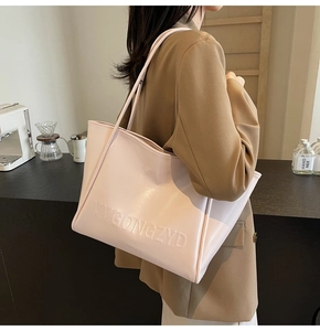 Dettaglio della borsa tote in pelle rosa chiaro con testo a rilievo e tracolla