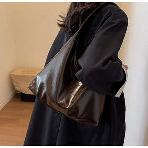 Détail du sac à bandoulière en cuir marron foncé brillant porté par un mannequin en intérieur