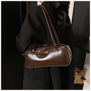 Deep brown patent leather baguette bag worn over the shoulder by a model for chic style