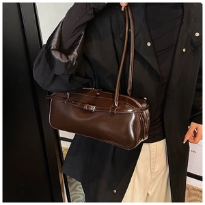 Detailed close-up of a glossy dark brown cylindrical baguette bag on a shoulder