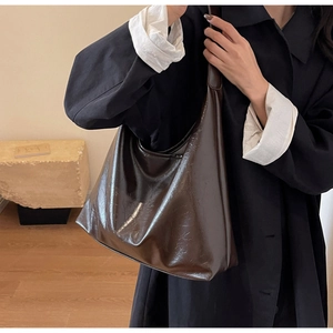Détail d'un grand sac Hobo en cuir ciré marron foncé porté à l'épaule par un mannequin