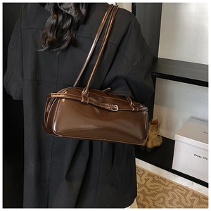 Brown glossy leather baguette bag with silver metal buckle on a model's shoulder
