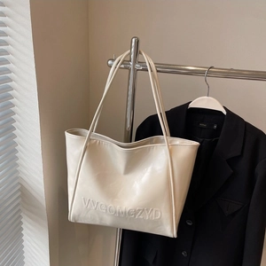 Grande borsa tote chic color crema con finitura lucida appesa a una gruccia nera