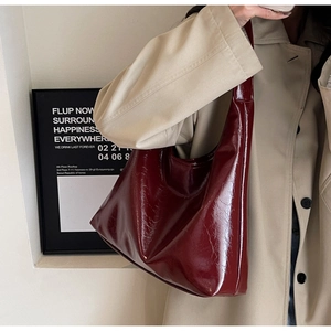 Détail d'un sac hobo en cuir verni rouge foncé porté avec un manteau beige chic