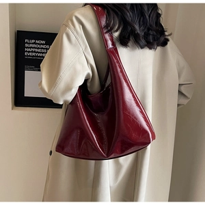 Détail d'un grand sac à bandoulière en cuir verni rouge foncé porté avec un trench beige