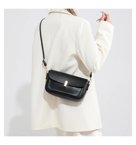 Close-up of black crossbody bag with gold lock buckle on white blazer outfit
