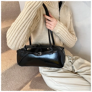 Glossy black baguette bag with metal buckle detail worn by a model in casual knitwear