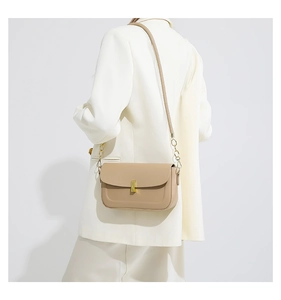 Detail of a chic cream leather crossbody bag with gold chain strap on a white suit model