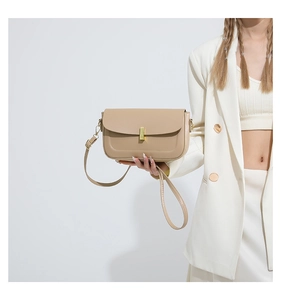 Detail of beige leather crossbody bag with golden clasp worn by model in suit