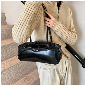 Detail view of black glossy baguette bag with metal buckle on model in cozy interior