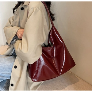 Détail du sac à main en cuir verni bordeaux brillant avec large bandoulière porté par mannequin